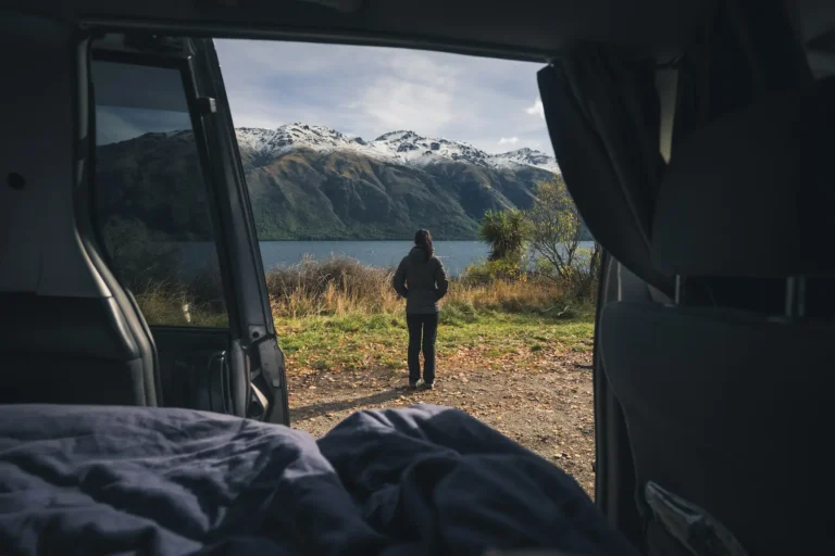 Mujer contemplando un lago desde el interior de su furgoneta camper